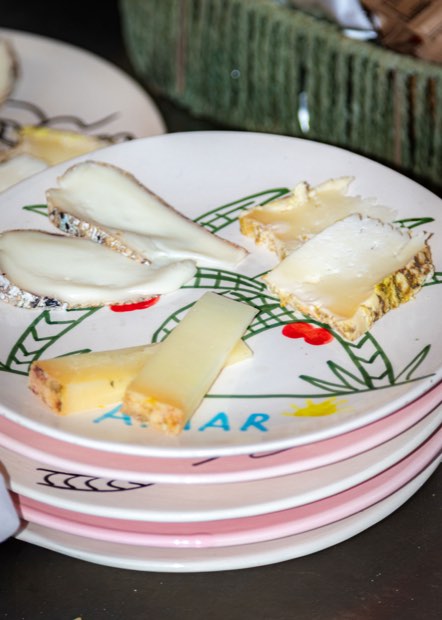 Una pila de platos de AMAR con borde rosa y tostadas con queso curado.