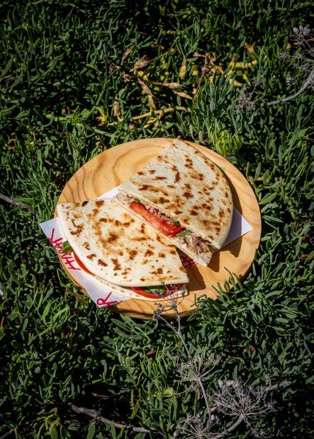 Dos piadinas dobladas sobre una tabla de madera apoyada en la vegetación baja de la playa.