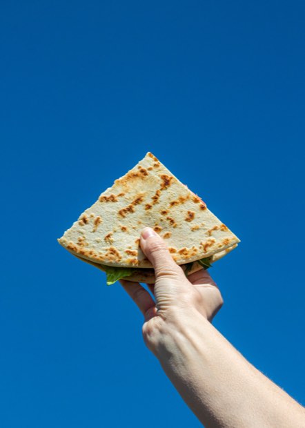 Una piadina doblada sostenida en alto contra un cielo azul intenso.