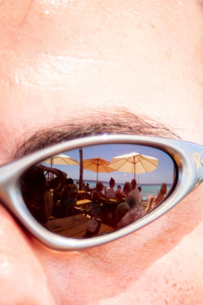 Primer plano de unas gafas de sol que reflejan las sombrillas y las mesas de la terraza.