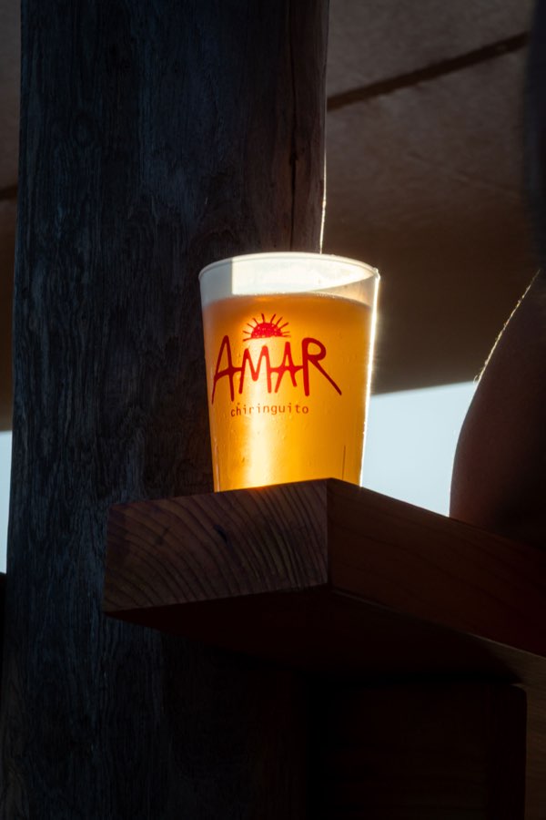 Una caña de cerveza con el sol del logo de AMAR, iluminada a contraluz por el sol bajo.