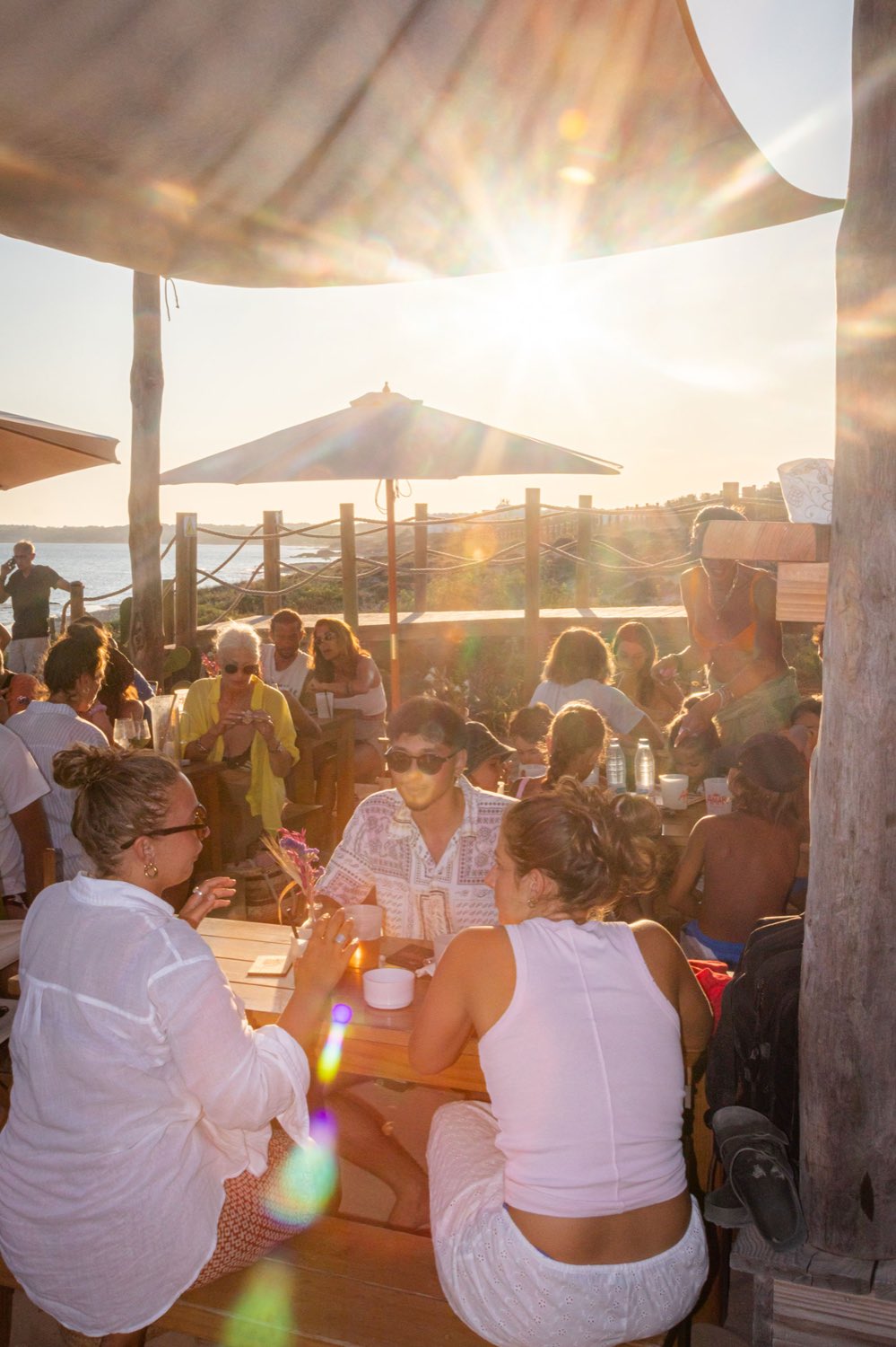 La terraza de AMAR al atardecer, con el sol destellando bajo entre las sombrillas sobre las mesas llenas.